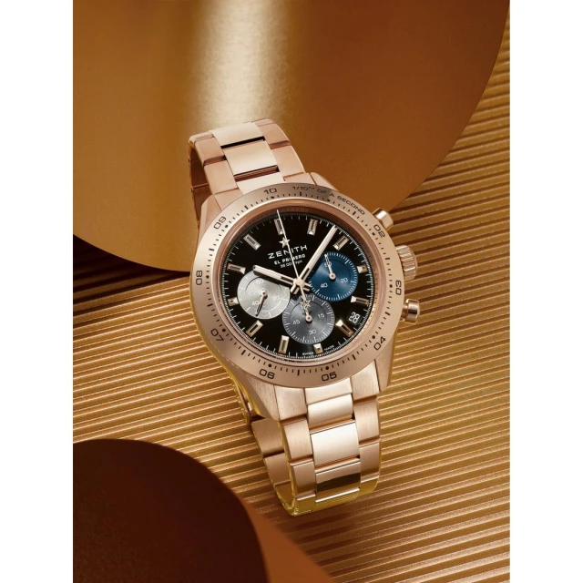 Rose gold Zenith watch with black dial and chronograph function on a shiny gold background, product shot for luxury timepieces.