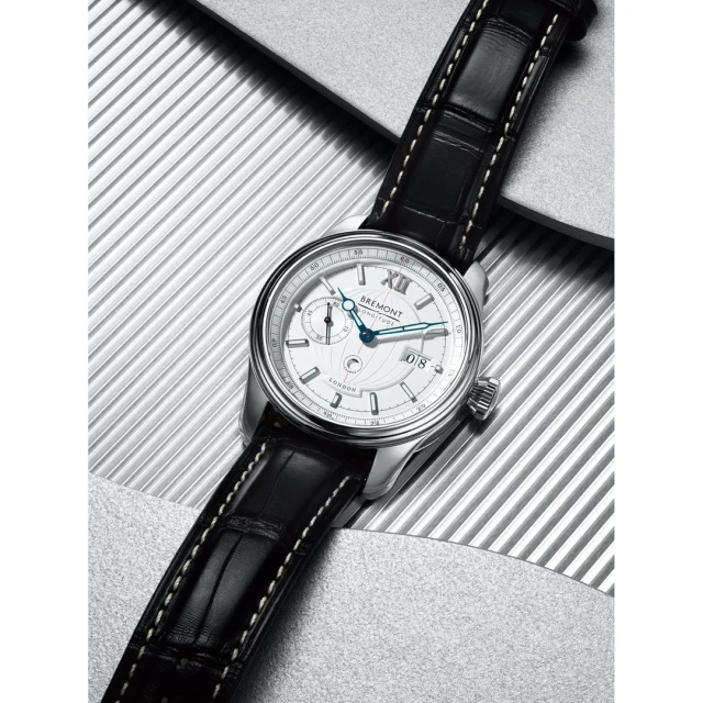 Silver Bremont wristwatch with a black leather strap, featuring a round white dial and a silver case, against a textured background.