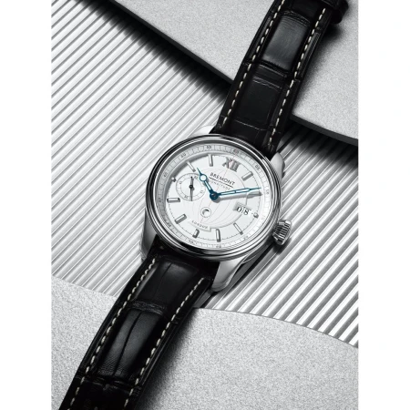 Silver Bremont wristwatch with a black leather strap, featuring a round white dial and a silver case, against a textured background.