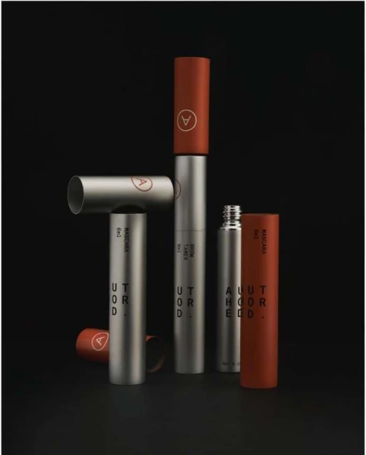 Still life of silver and red-brown cosmetic tubes and containers with visible text and logos on a dark black background.