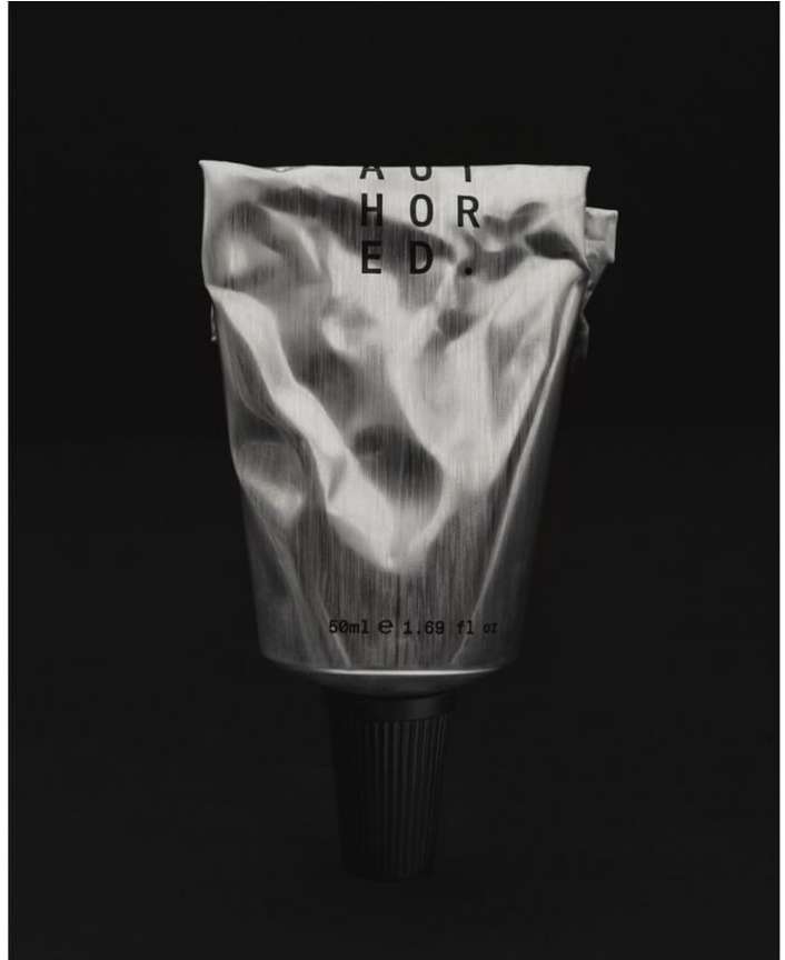 Still life photograph of a silver tube of cream or lotion with black lettering, centered on a black background.