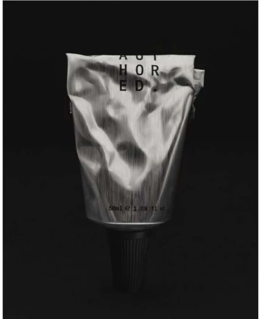 Still life photograph of a silver tube of cream or lotion with black lettering, centered on a black background.