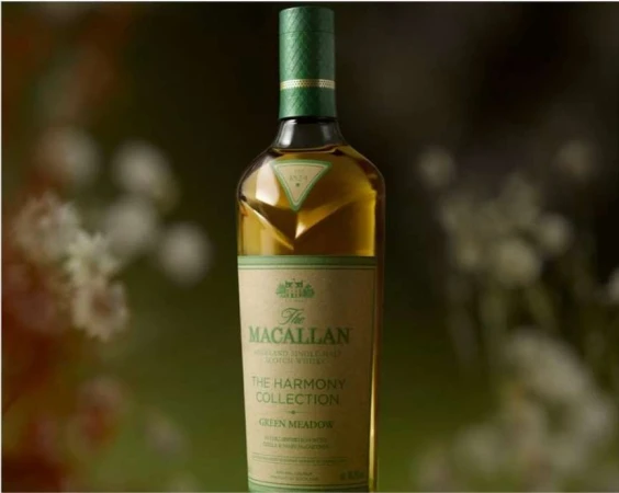 A bottle of The Macallan Harmony Collection Green Meadow whisky stands centered against a blurred floral background, highlighting its green labeling.