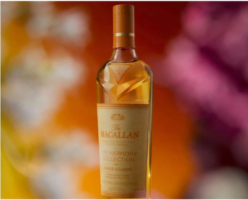 Close-up shot of a bottle of The Macallan Harmony Collection Amber Meadow whisky against a blurred, colorful background. 