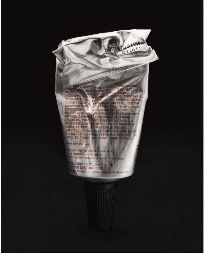 Silver tube of tinted moisturizer with black cap. Close-up product shot on dark background emphasizing the texture and packaging.