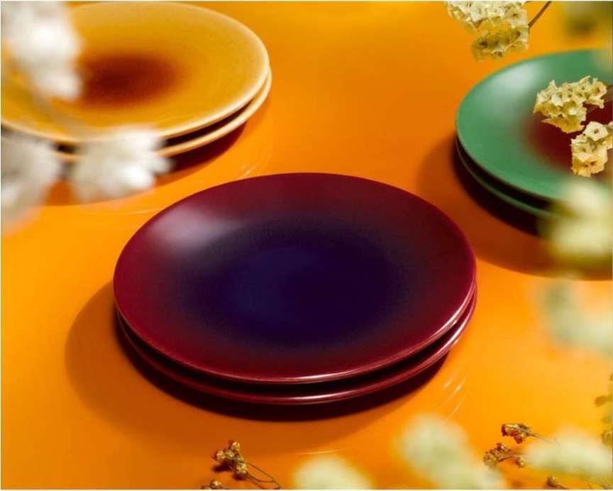 Stack of colorful ceramic plates on an orange surface with diffused light, creating a warm and inviting culinary display.