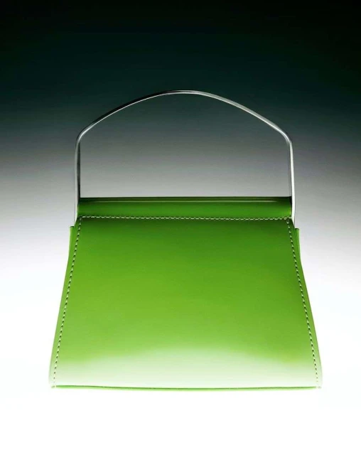 A green patent leather handbag with a metal handle is centered in a studio shot against a gradient gray background.