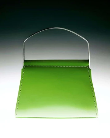 A green patent leather handbag with a metal handle is centered in a studio shot against a gradient gray background.