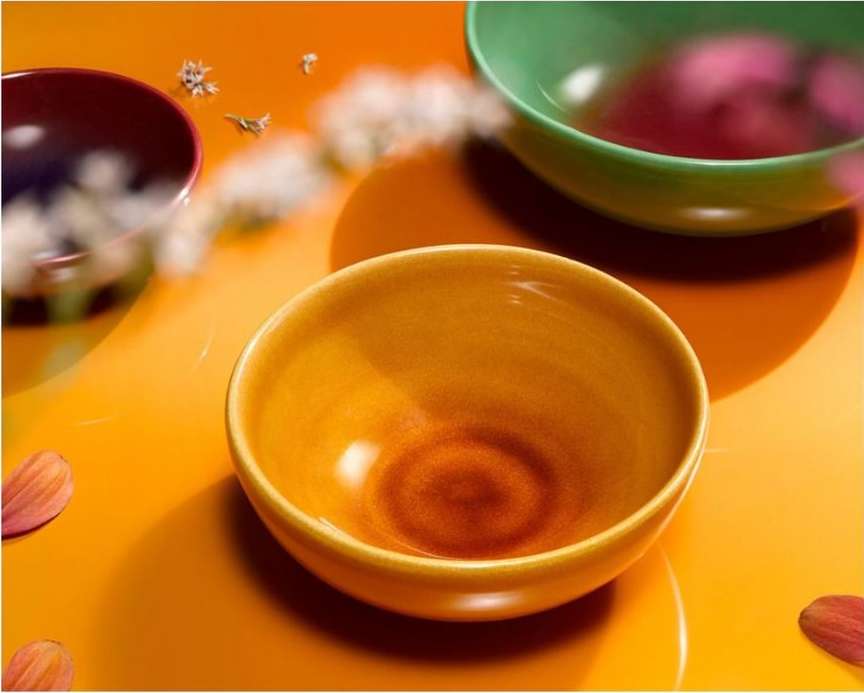 Still life image with three colorful ceramic bowls on an orange surface, complemented by scattered petals and small white flowers.