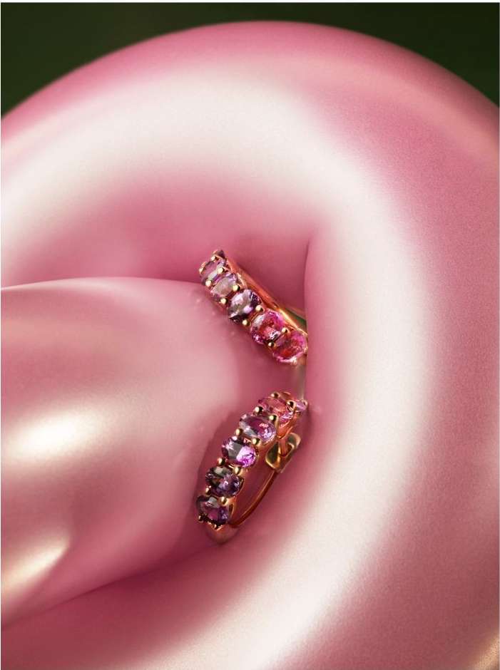 Close-up of a pair of gold hoop earrings with multiple pink and purple gemstones, set against a softly blurred pink background.