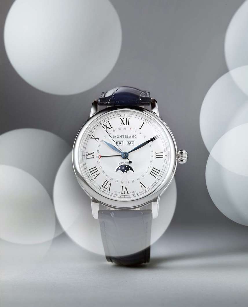 Silver Montblanc wristwatch with black leather strap against a grey background with out-of-focus lights, showcasing luxury timekeeping.
