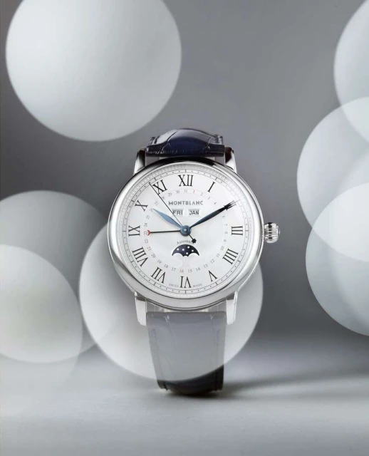 Silver Montblanc wristwatch with black leather strap against a grey background with out-of-focus lights, showcasing luxury timekeeping.