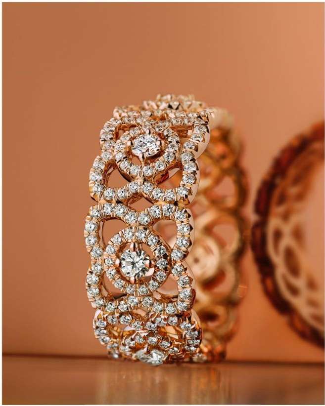 Ornate gold ring with diamonds on a tan surface, featuring an intricate pattern and a shallow depth of field emphasizing its detailed design.