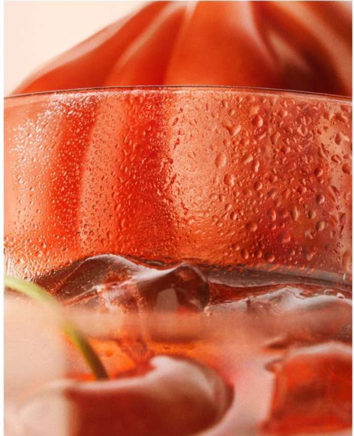 Close-up of a glass filled with a red drink and ice, garnished with a cherry, highlighting condensation and vibrant color.