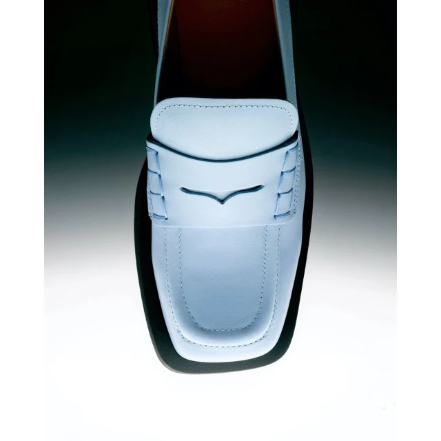 Overhead shot of a single light blue leather loafer shoe against a blended gradient dark to light background. Elegant and minimalist.