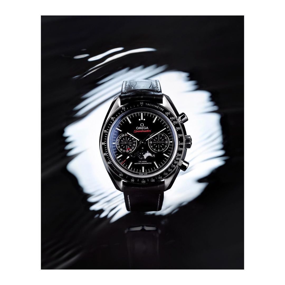 Omega Speedmaster watch on a black reflective surface, accentuated by a swirling white light pattern creating a dramatic contrast.
