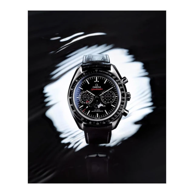 Omega Speedmaster watch on a black reflective surface, accentuated by a swirling white light pattern creating a dramatic contrast.