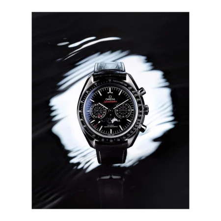 Omega Speedmaster watch on a black reflective surface, accentuated by a swirling white light pattern creating a dramatic contrast.