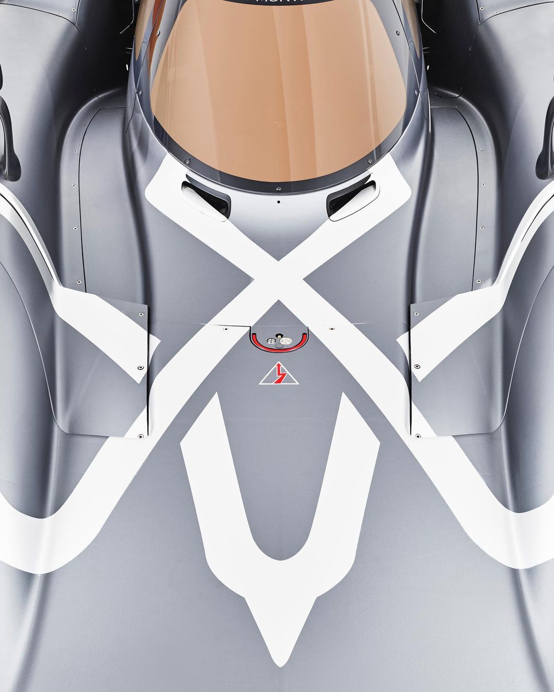 Overhead view of a gray race car with white stripe designs on its hood and windshield, showcasing an aerodynamic design.