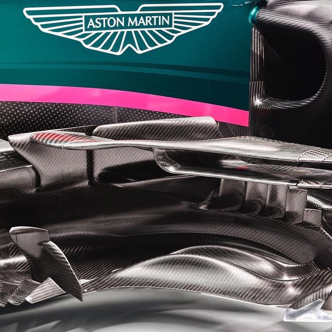 Close-up of the carbon fiber front of an Aston Martin racing car with logo on dark green and pink background, racing car components.