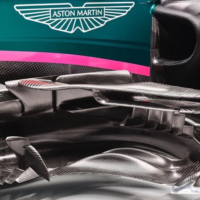 Close-up of the carbon fiber front of an Aston Martin racing car with logo on dark green and pink background, racing car components.