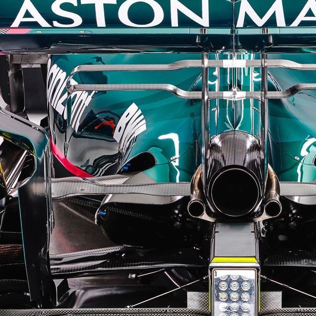 Close-up of a turquoise and black Aston Martin Formula One race car showcasing the rear end with exhaust pipes and lighting.