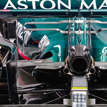 Close-up of a turquoise and black Aston Martin Formula One race car showcasing the rear end with exhaust pipes and lighting.
