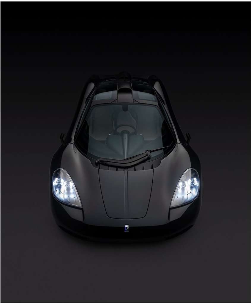 Overhead shot of a black sports car with headlights on, displayed against a dark background in a studio setting, showcasing sleek design.