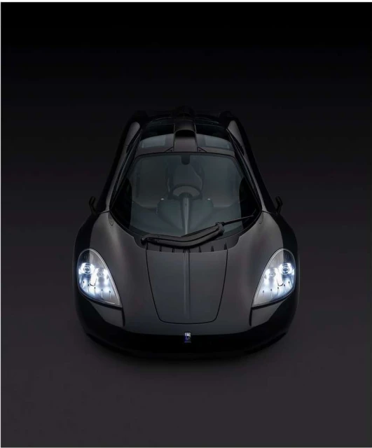 Overhead shot of a black sports car with headlights on, displayed against a dark background in a studio setting, showcasing sleek design.
