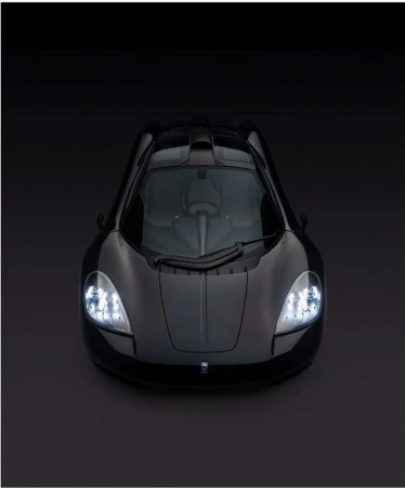 Overhead shot of a black sports car with headlights on, displayed against a dark background in a studio setting, showcasing sleek design.