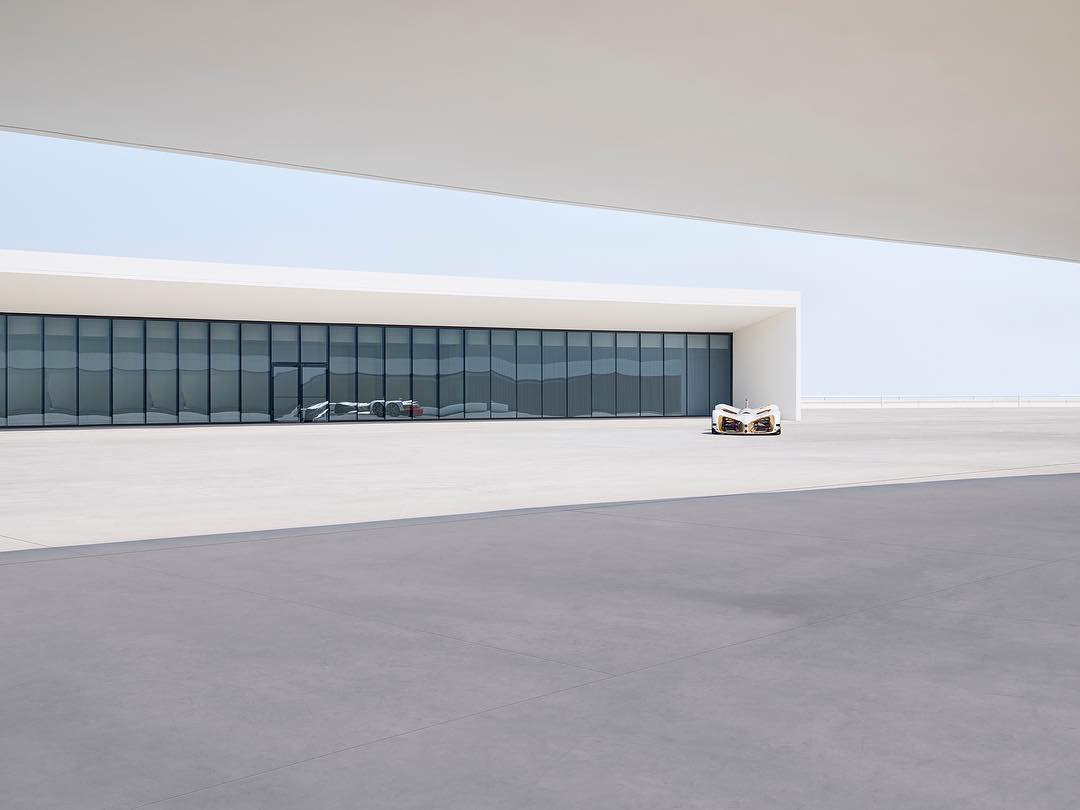 Front view of a white supercar parked in front of a modern building with glass windows on a light grey concrete surface.