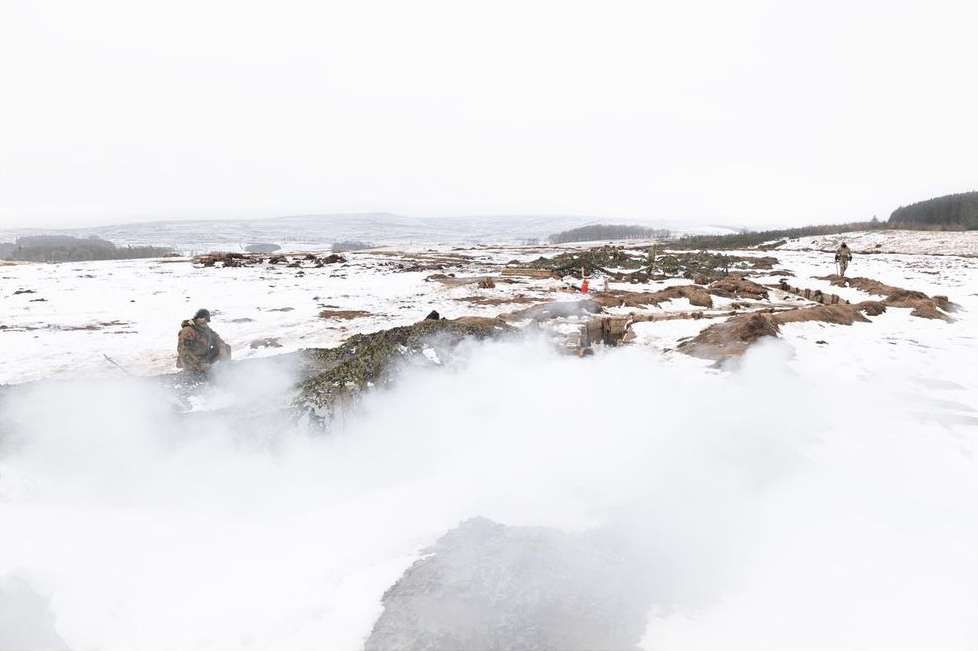 Military personnel in camouflage gear are positioned in a snowy, outdoor environment with fog, possibly during a training exercise or operation.