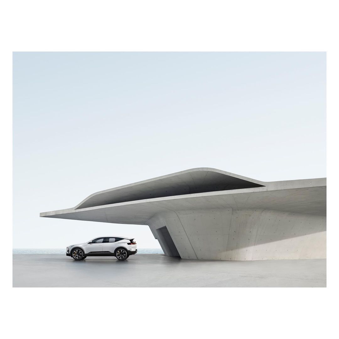 Modern white SUV car parked beneath a contemporary concrete architectural structure against a light blue sky, showcasing minimalist automotive design.