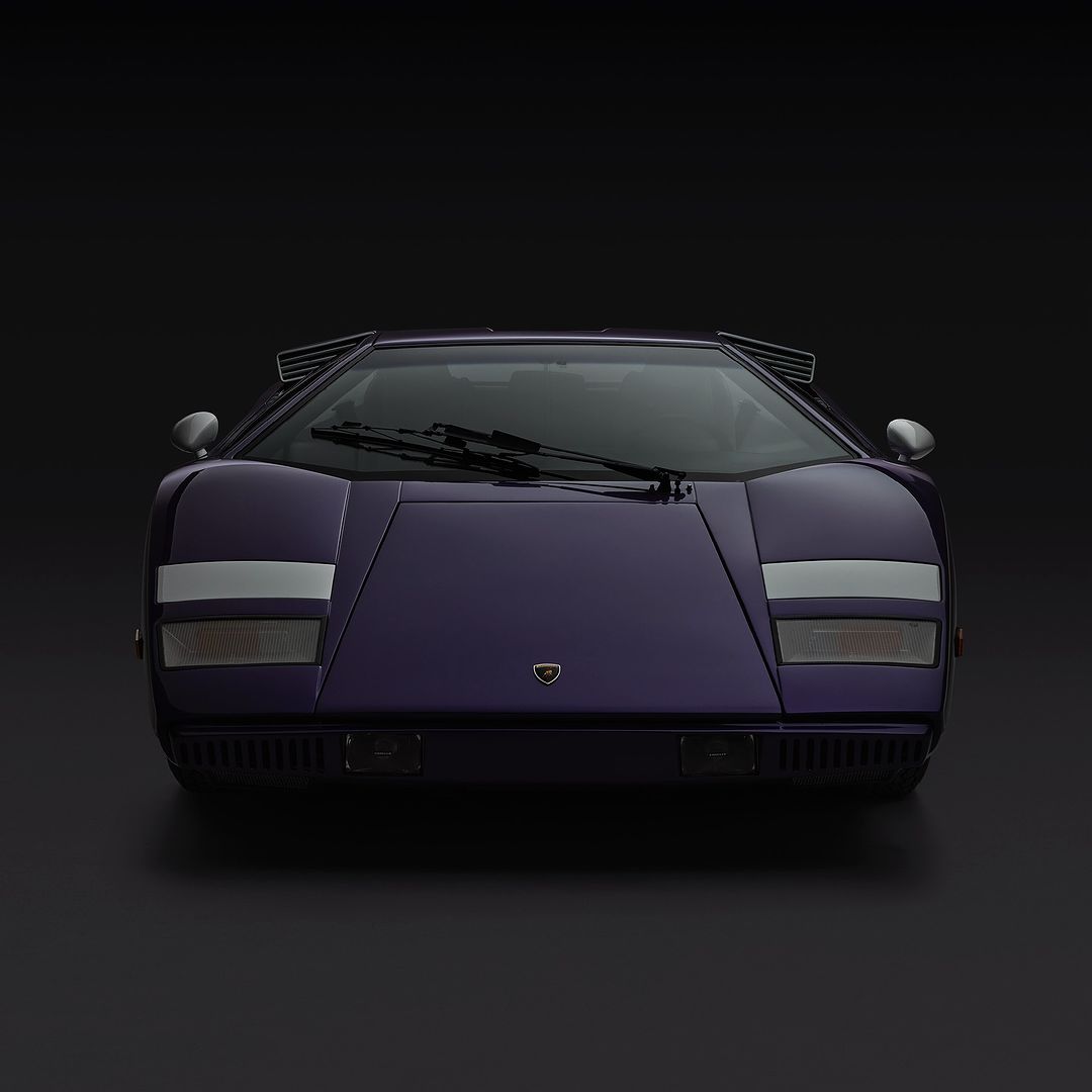 Frontal view of a purple Lamborghini Countach against a dark background, showcasing its iconic wedge shape and distinctive styling.