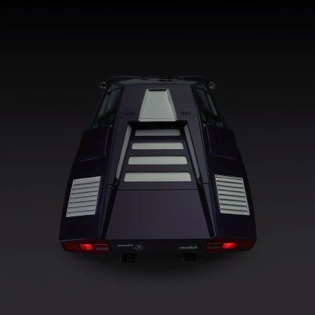 Rear view of a purple Lamborghini Countach with silver trim against a dark background, highlighting its angular design and taillights.