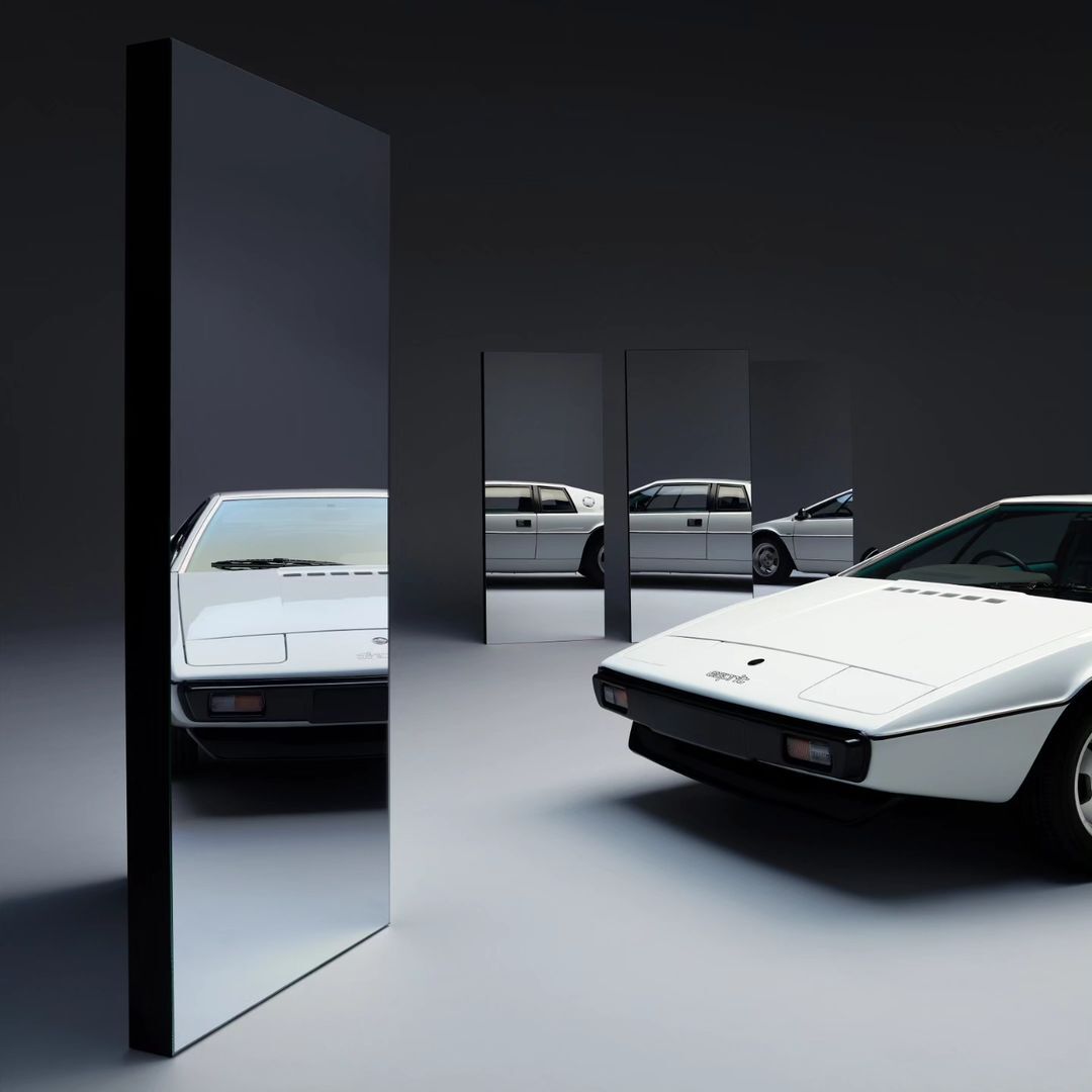 A sleek white Lotus Esprit automobile is showcased in a minimalist photo studio setting, flanked by reflective black panels.