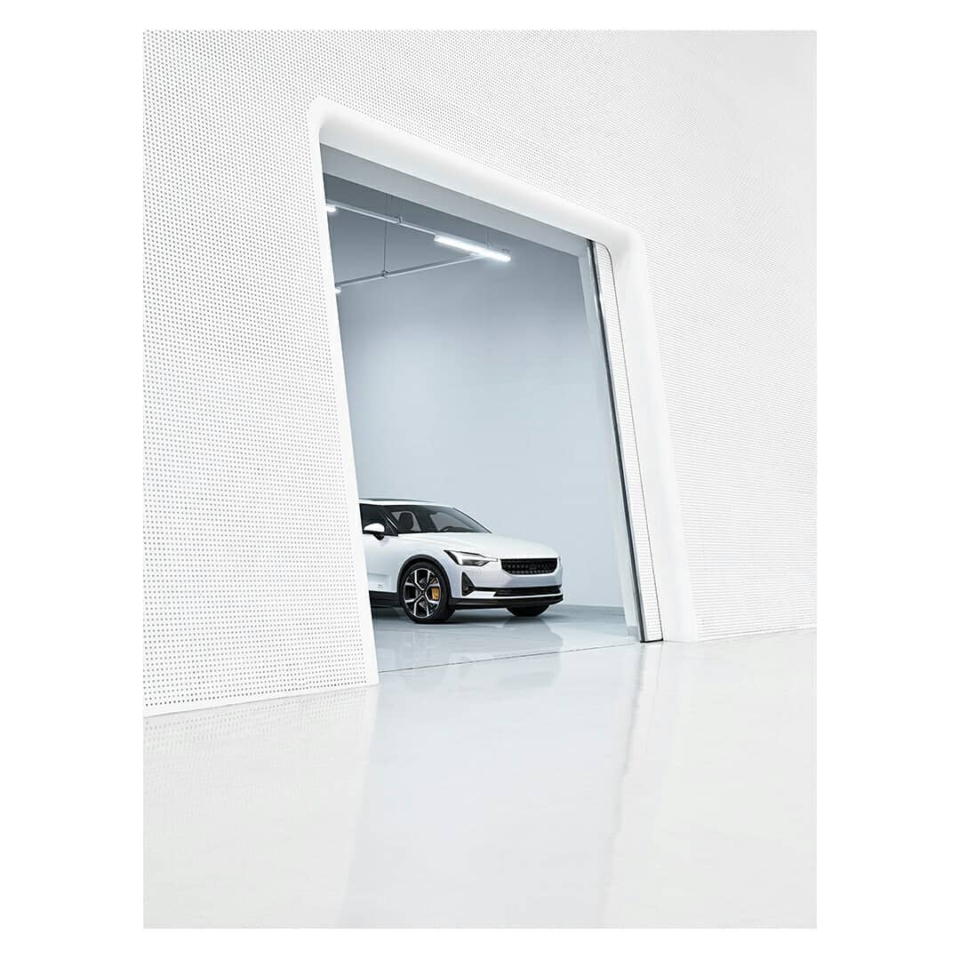 Sleek white Polestar electric car showcased in a bright, minimalist garage with dotted textured walls and reflective flooring.