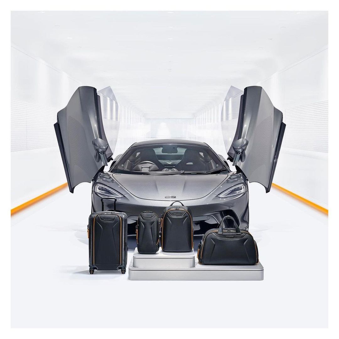 Sleek gray McLaren sports car showcased with matching luggage set in a bright studio, emphasizing luxury automotive lifestyle.