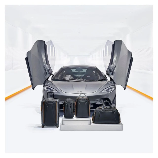 Sleek gray McLaren sports car showcased with matching luggage set in a bright studio, emphasizing luxury automotive lifestyle.