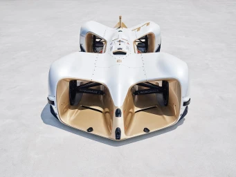 High-angle view of an autonomous electric race car in white and gold finish parked on a seamless light grey ground
