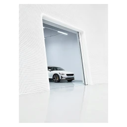 White electric car parked inside a bright modern studio garage viewed through a large white portal aperture.