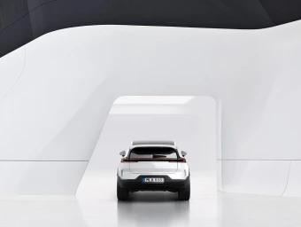 Rear view of a white car parked inside a modern minimalist white architectural structure with curved openings.