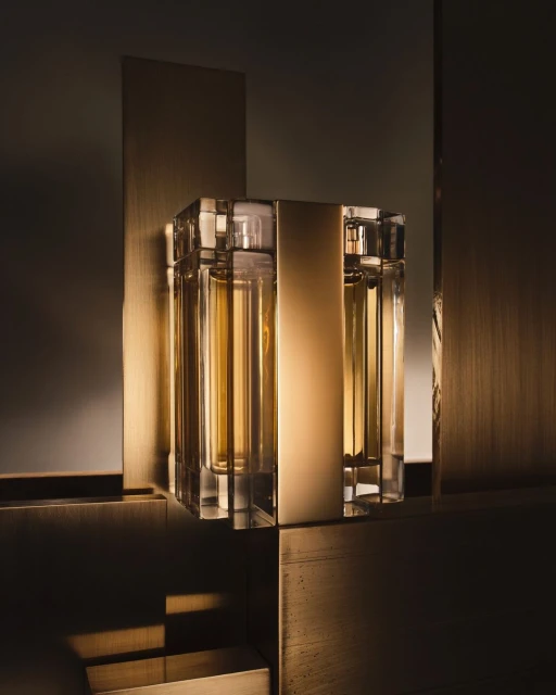 Crystal perfume bottle with golden liquid stands on a gold and dark bronze geometric surface, showcasing luxury and geometric composition.