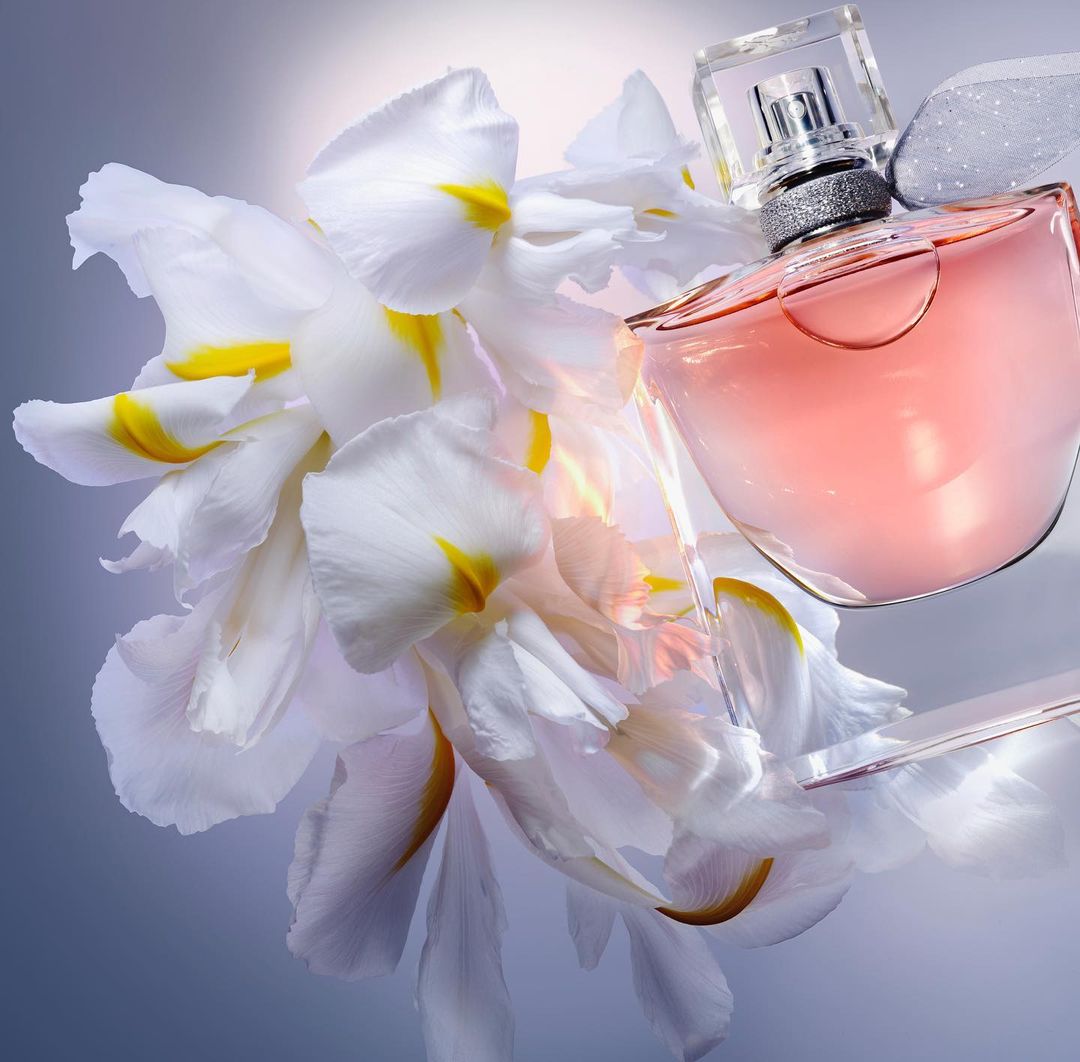 Fragrant perfume bottle presented with white iris flowers on a soft, diffused studio backdrop creating an elegant cosmetic still life.