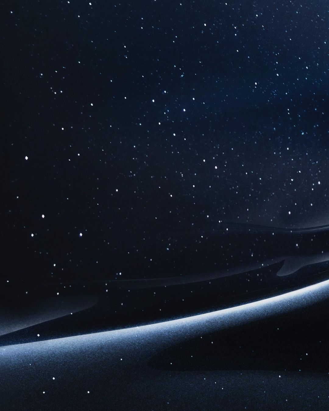 Night sky abstract background featuring a gradient of deep blues and blacks with a luminous band and scattered, bright starlike points.
