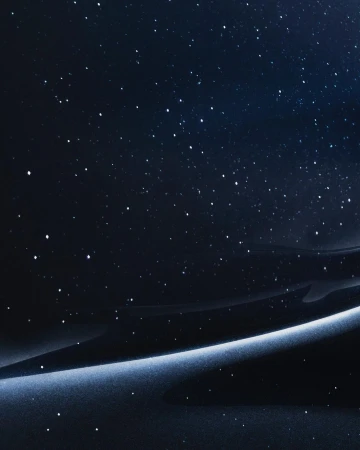 Night sky abstract background featuring a gradient of deep blues and blacks with a luminous band and scattered, bright starlike points.