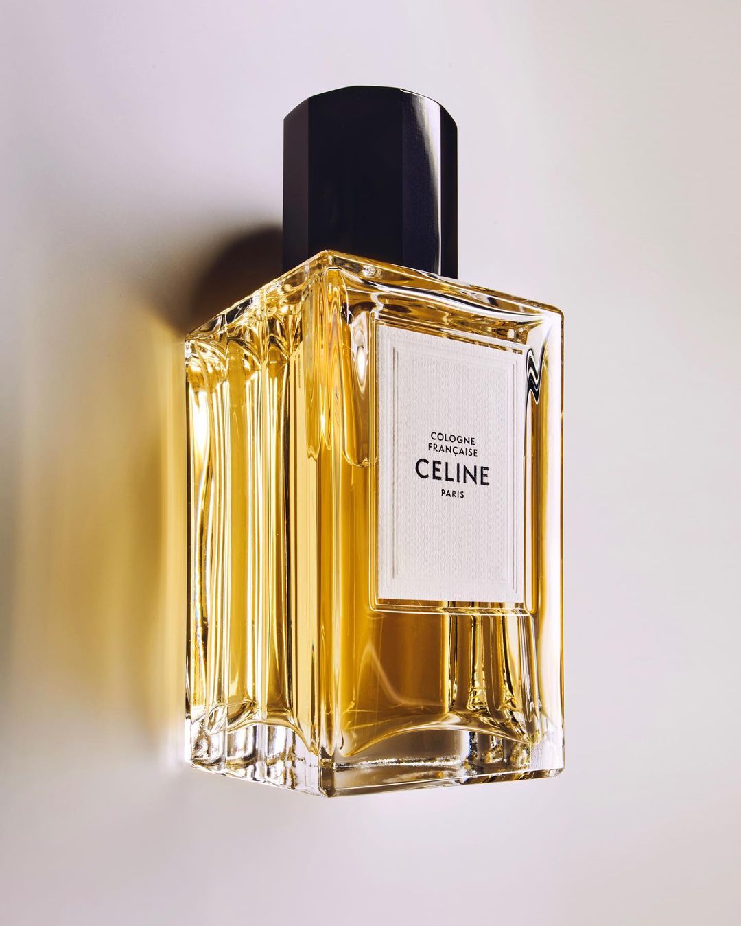 Celine cologne bottle stands prominently, featuring a black cap, transparent glass, and minimalist label against a gradient background.