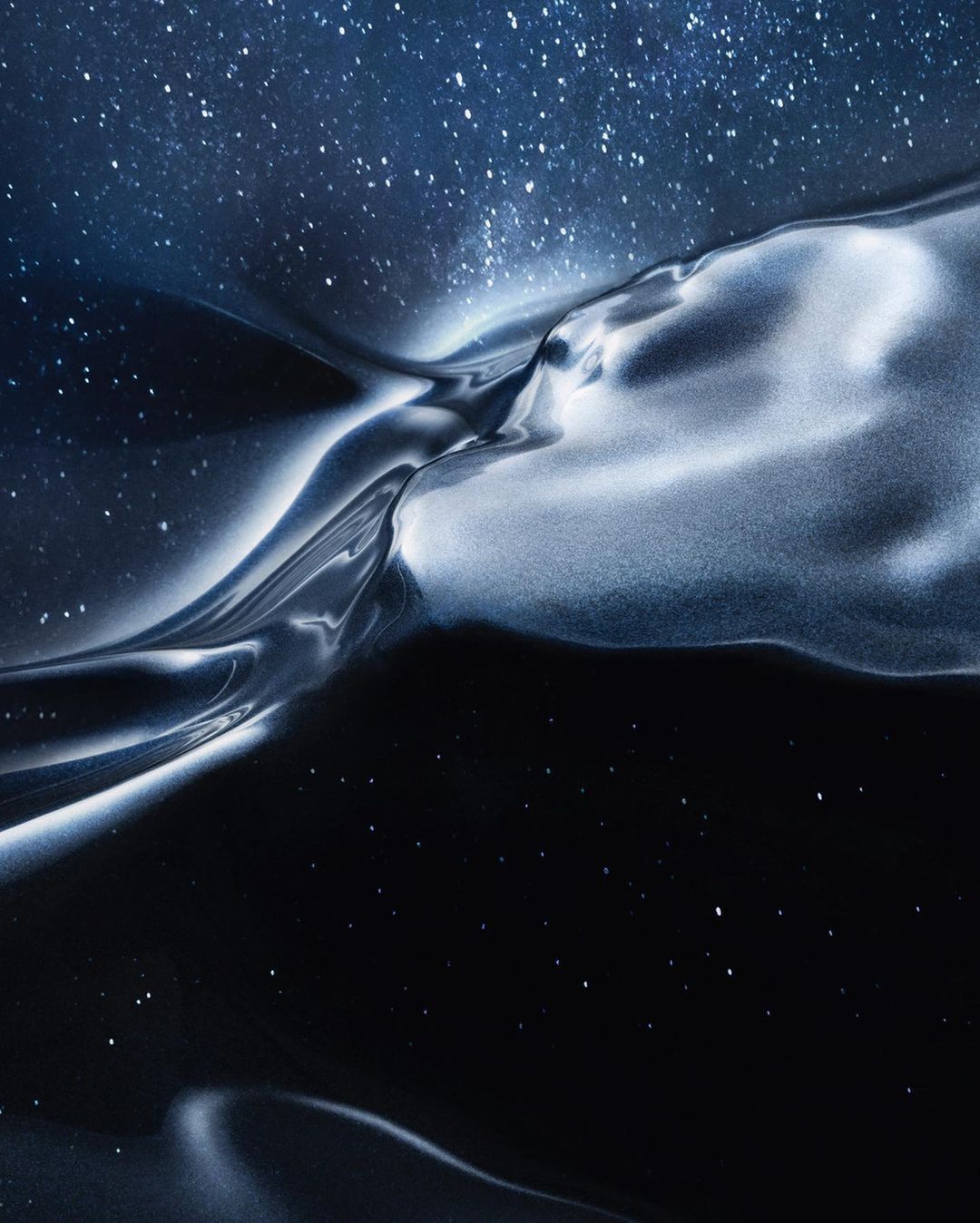 Abstract image of a reflective, fluid-like texture in shades of silver and black set against a backdrop of a blue, star-filled sky.