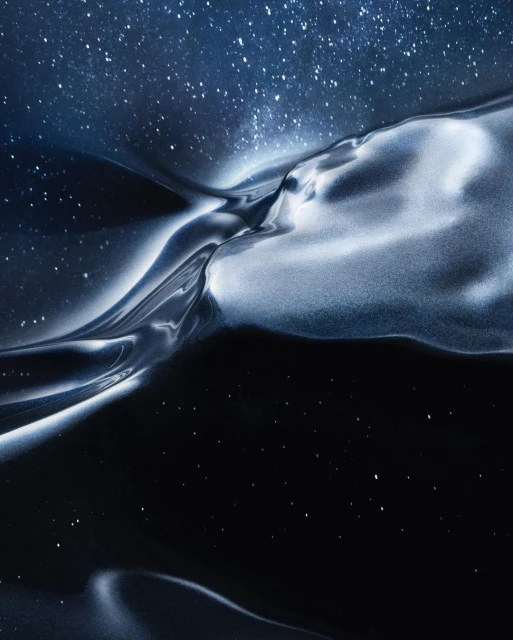Abstract image of a reflective, fluid-like texture in shades of silver and black set against a backdrop of a blue, star-filled sky.