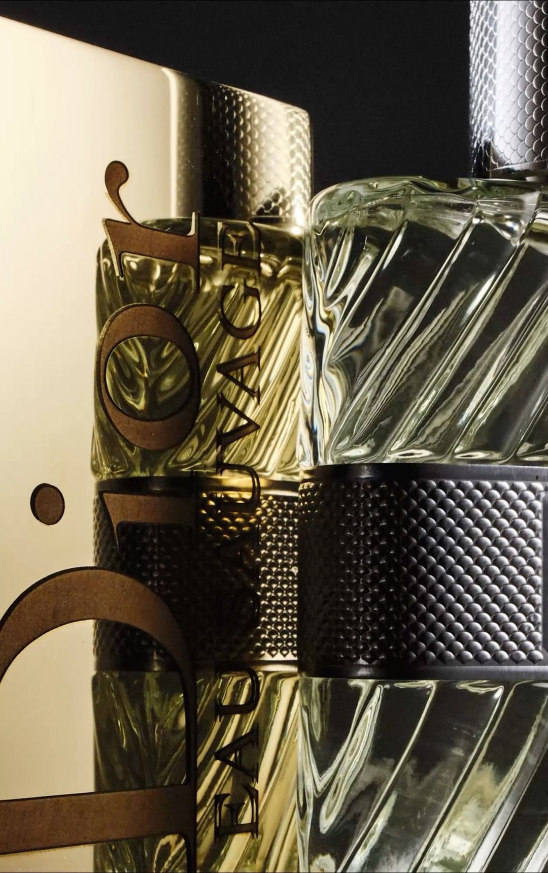 Multiple textured glass and gold bottles of perfume stacked on top of each other in a studio setting, illuminated with dramatic lighting.